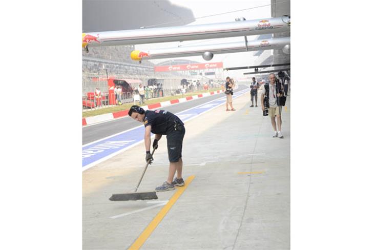 A Red Bull team member dusts the pit spot to ensure a clean getaway.