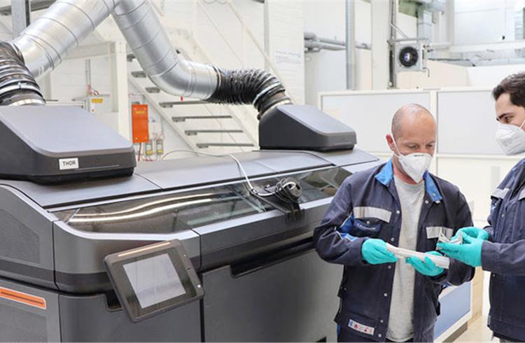 Two Volkswagen staffers check the quality of structural parts produced using the binder jetting process for car production in front of the prototype of the special printer in Wolfsburg.