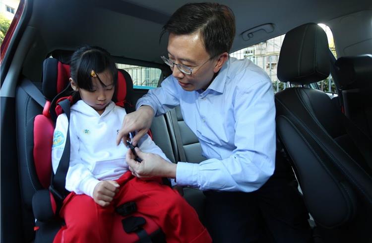 GM executive VP and GM China president Matt Tsien demonstrates the proper use of child safety seats and helps a child buckle up.