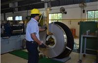 A staffer loads a wide band of steel under a slitter, which is the very first step in the process of manufacturing clamps.