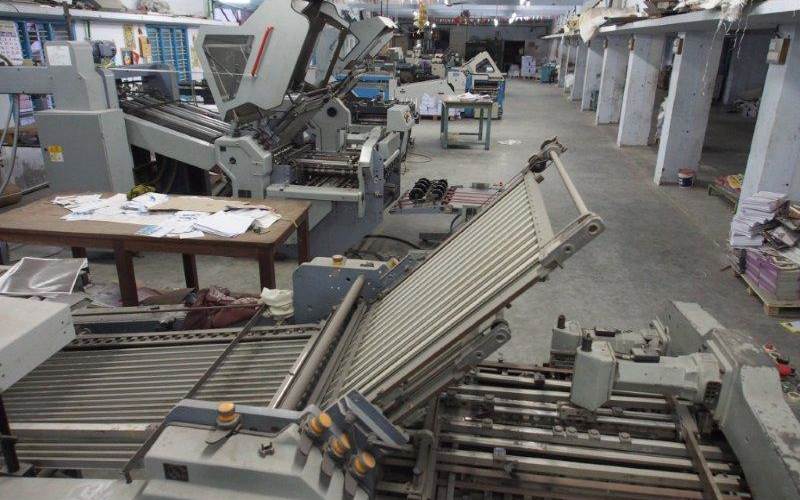 Photograph of a raft of paper folding machines during a change of shift..